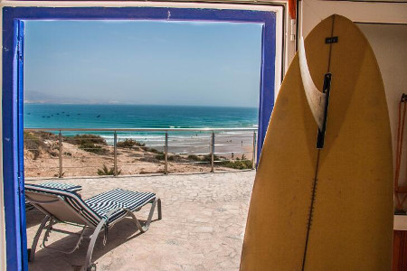 A surfboard by a doorway looking out onto the porch and the beach.